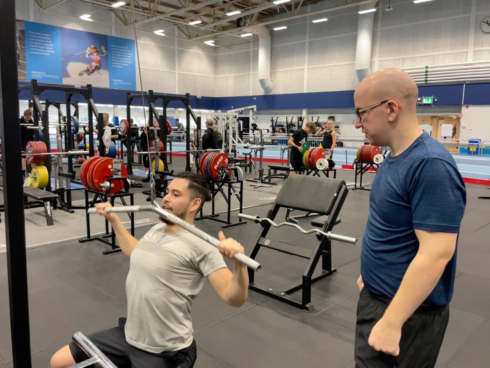 En PT instruerar en student i axelpress i Framgångshallen på Bosön