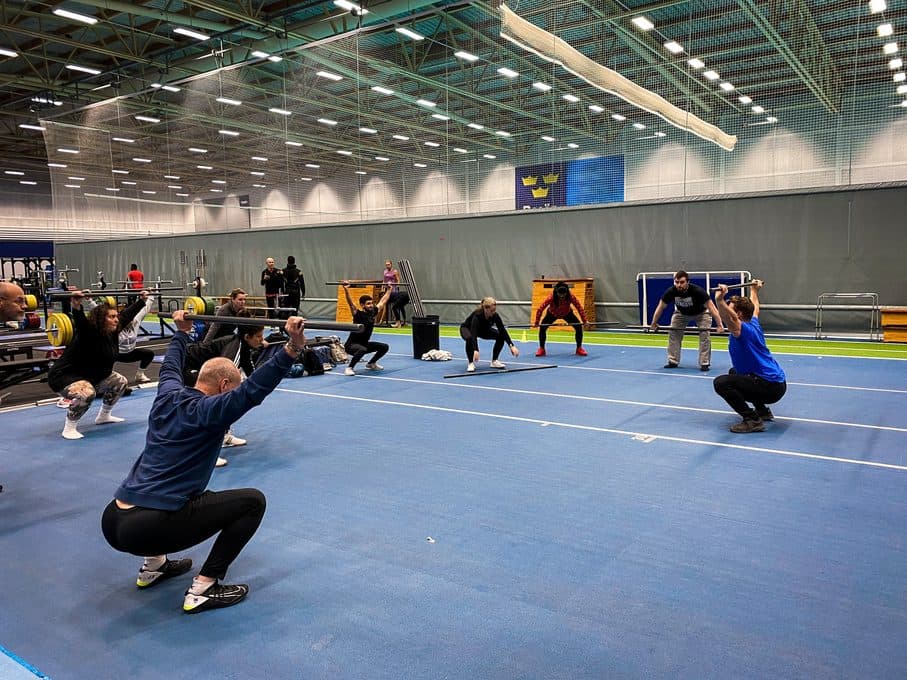 Klassen övar knäböj och positioner med lätta stänger i hallen